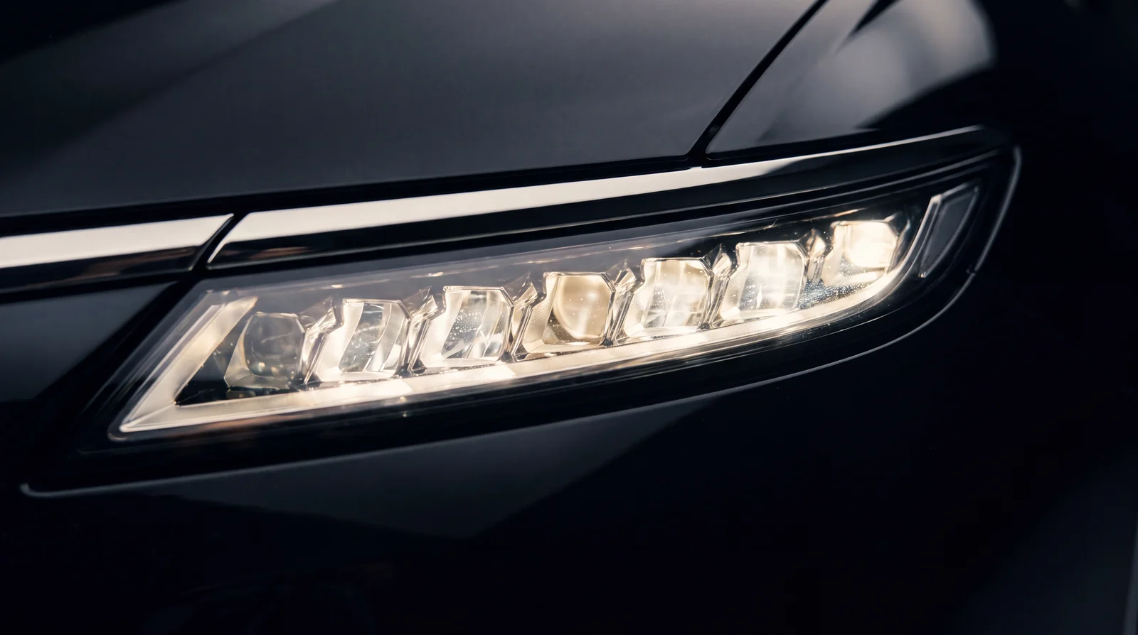 Macro detail of an illuminated slim LED headlight on black bodywork.