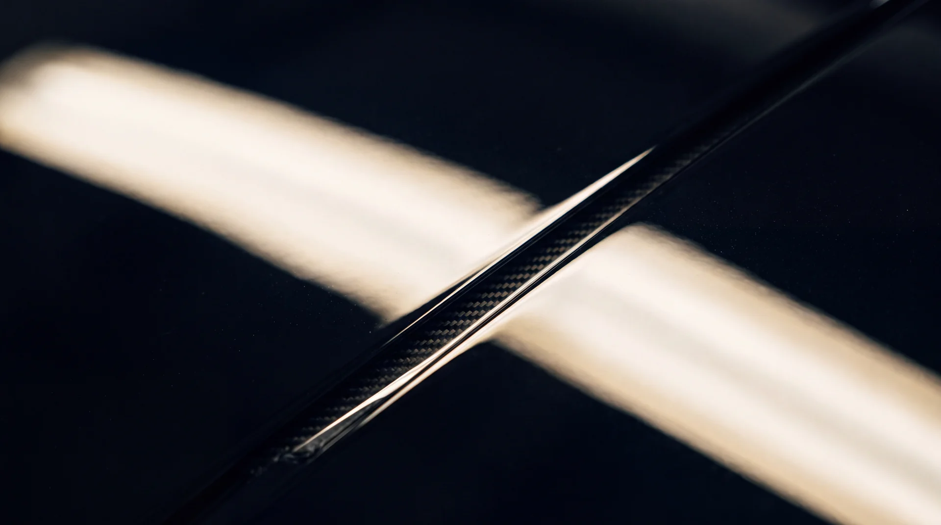 Extreme close-up of black car bodywork under a moving band of light.